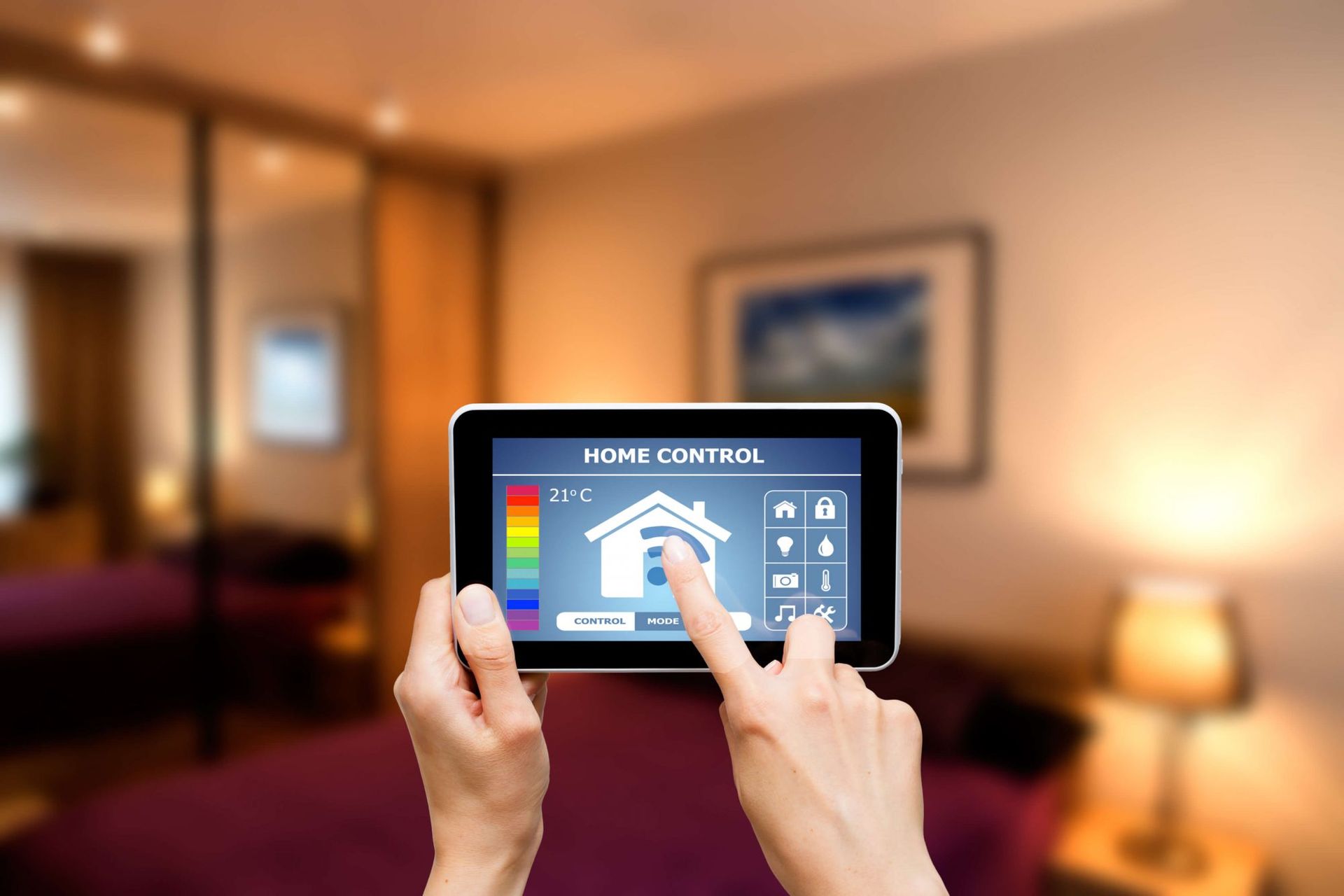 Des mains manipulent une tablette pour contrôler un écran domotique dans un salon à l'ambiance chaleureuse et légèrement floue.