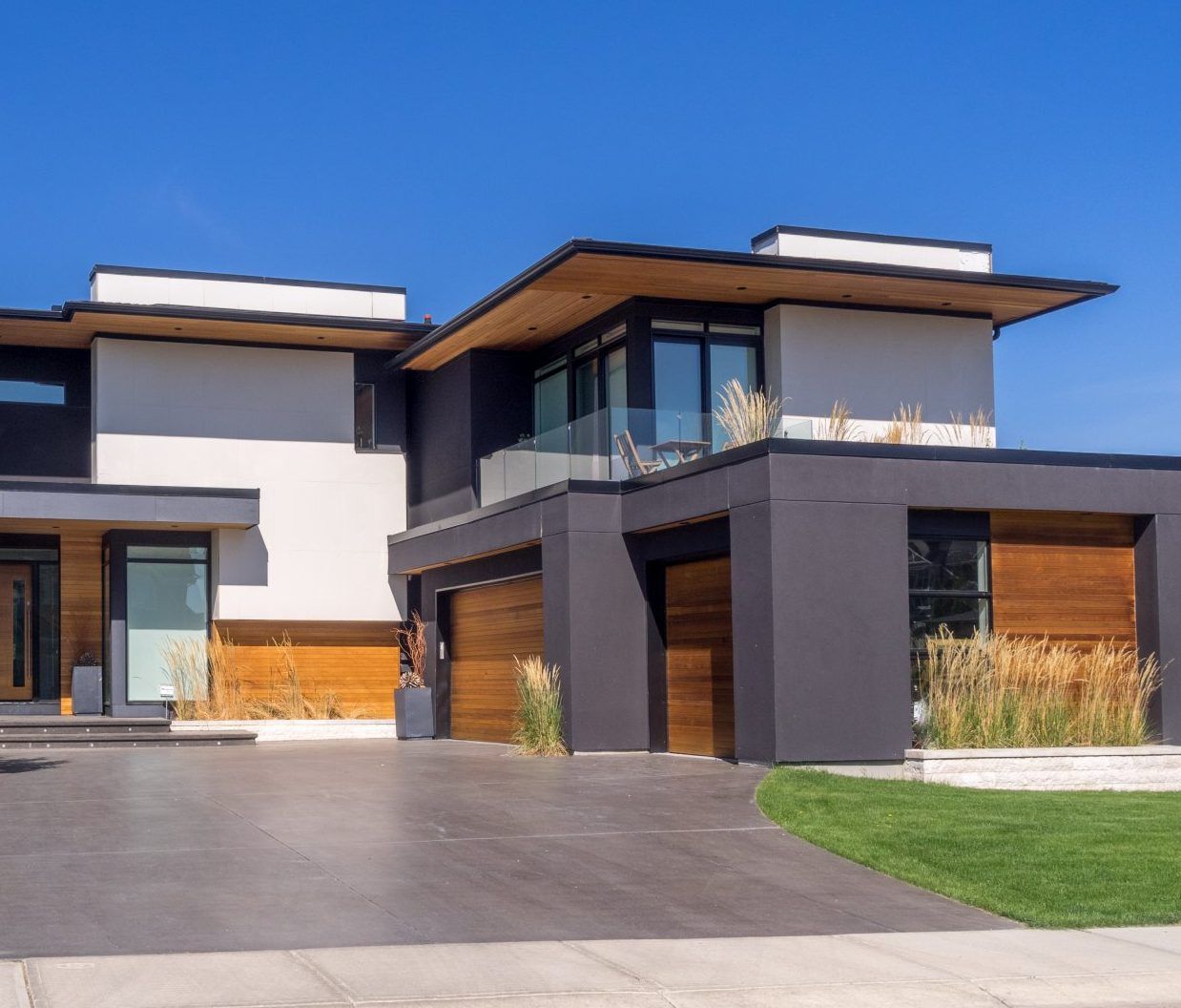 Maison moderne à deux étages avec extérieur blanc et gris foncé, accents de bois et allée sous un ciel bleu