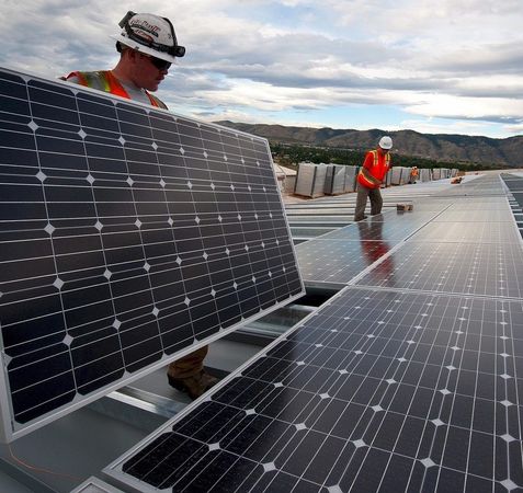 Des ouvriers installent des panneaux solaires sur un toit sous un ciel nuageux