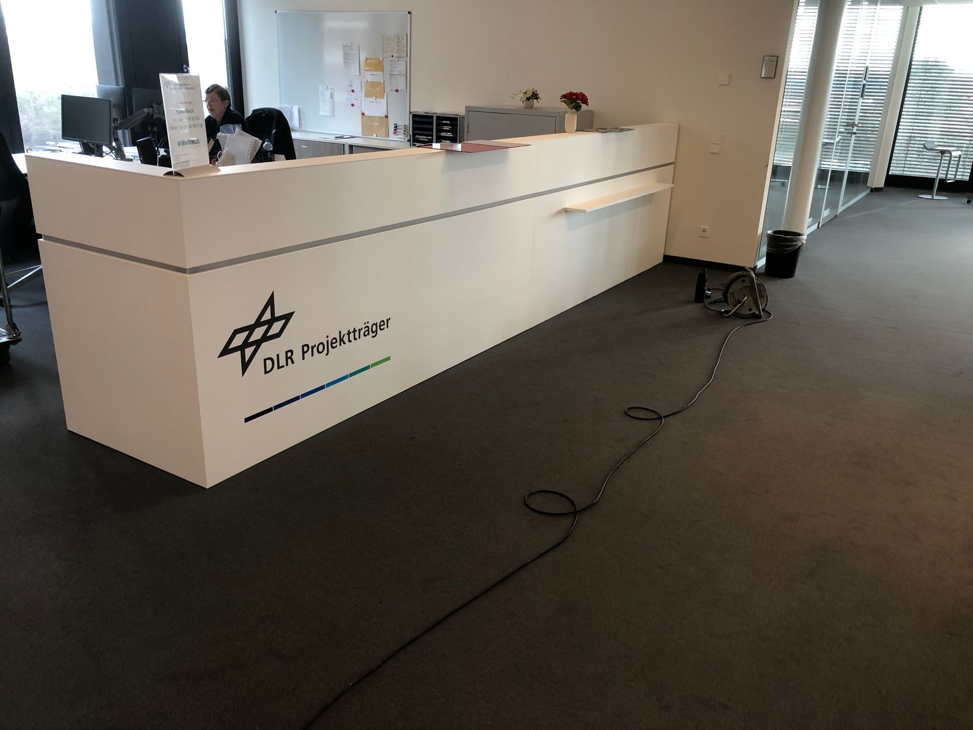 Eine Frau sitzt an einem Schreibtisch in einem Büro mit einem Schild mit der Aufschrift „DLP“