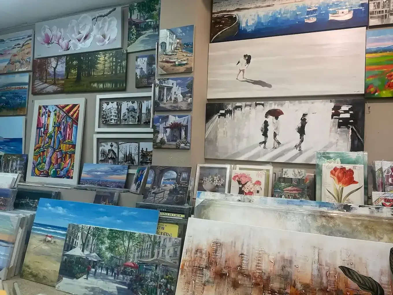 Diversos cuadros enmarcados y lienzos impresos expuestos en una pared y en estanterías de una galería de arte o tienda.
