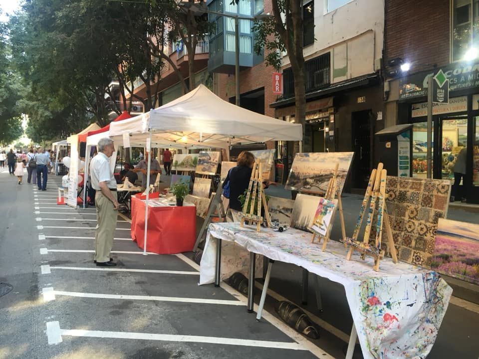 Una feria de arte callejero al aire libre con puestos con toldos blancos y cuadros expuestos en caballetes a lo largo de la acera.