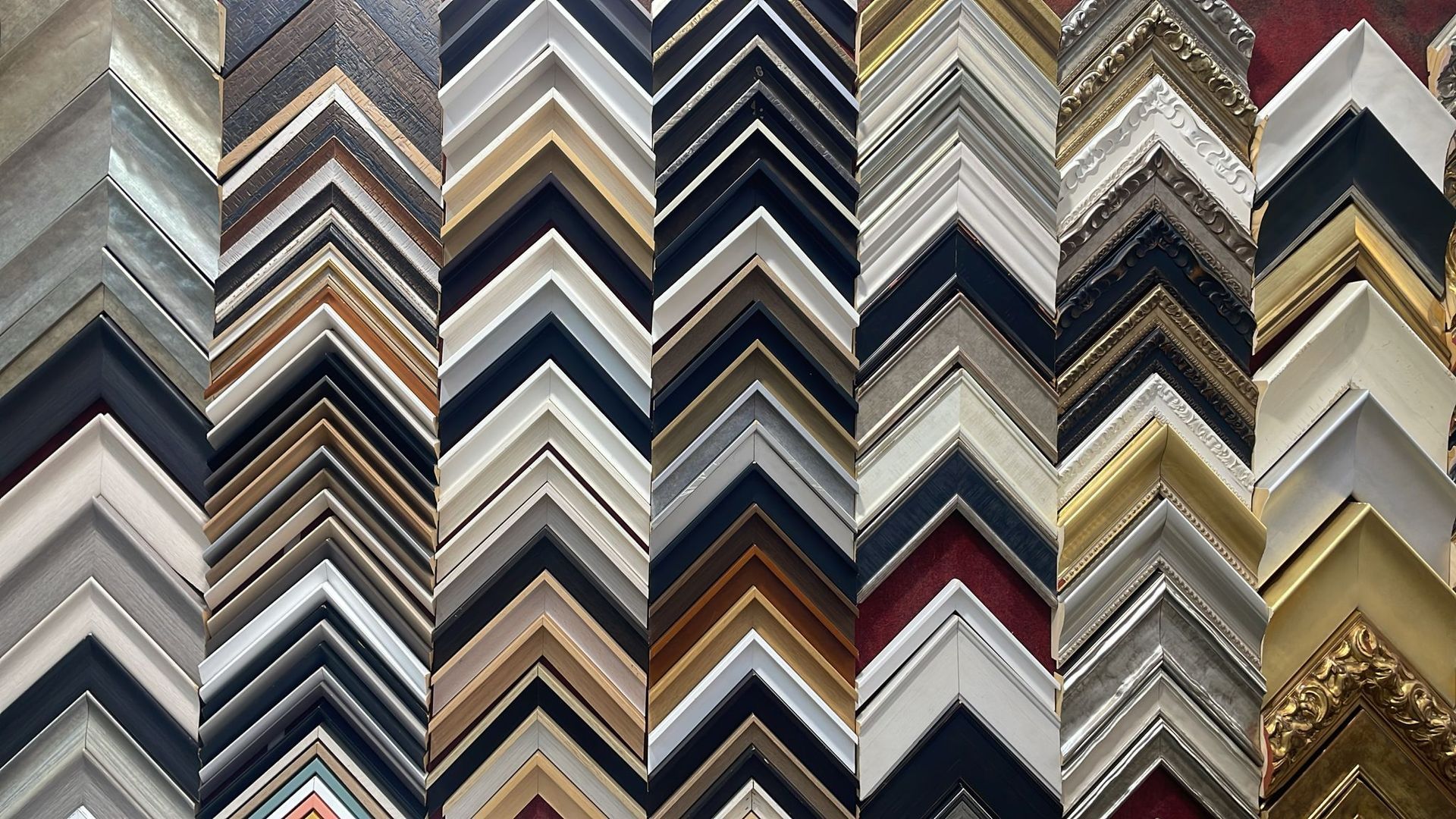 Una pared exhibe numerosas muestras de esquineras para marcos de fotos de madera, con diversos colores, texturas y estilos.