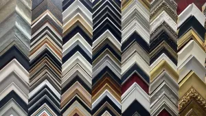 Una variedad de muestras de molduras para marcos de fotos, dispuestas verticalmente en filas de diferentes colores, texturas y estilos.