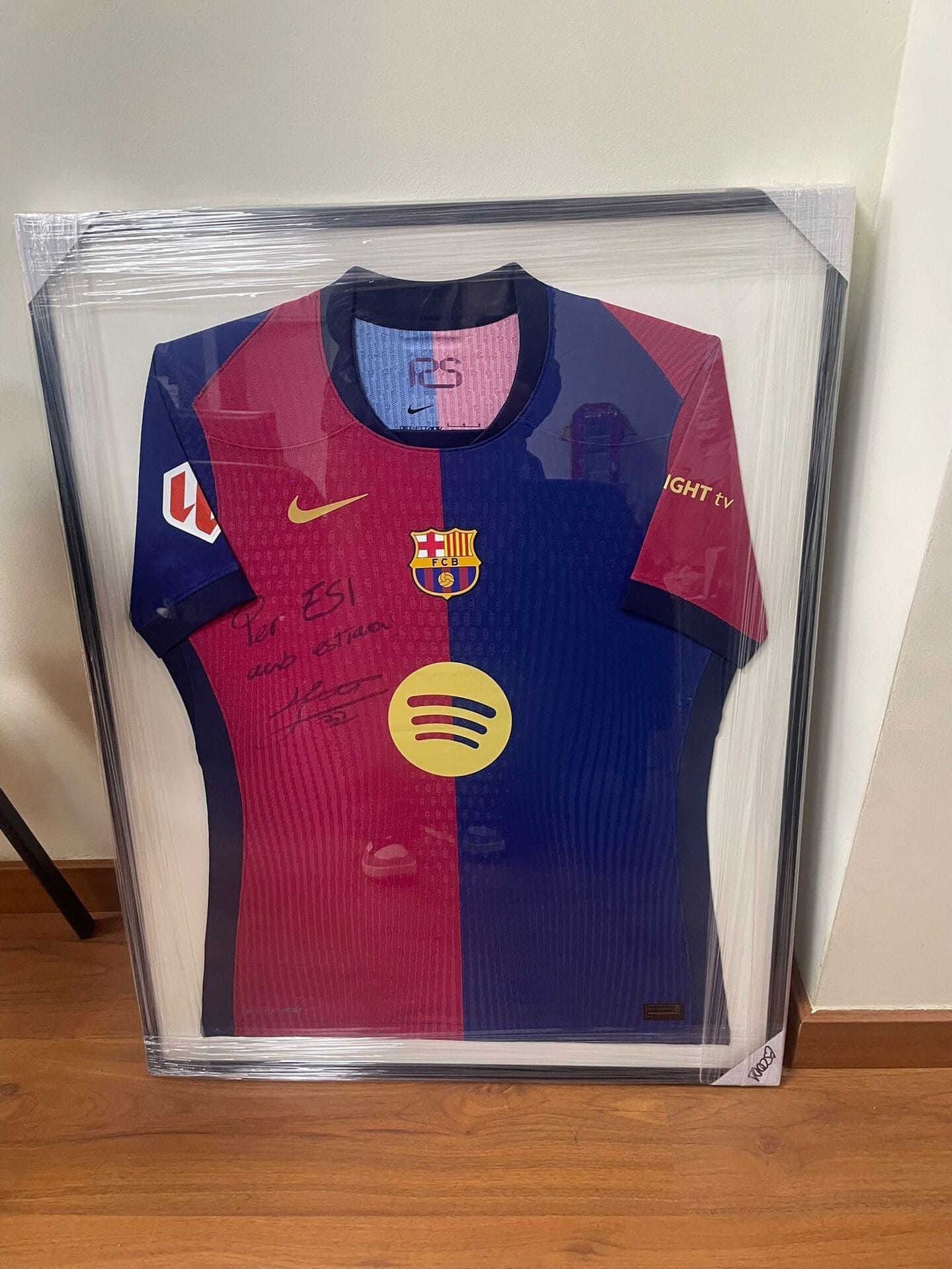 Camiseta del FC Barcelona enmarcada, de color rojo y azul, expuesta sobre un suelo de madera.