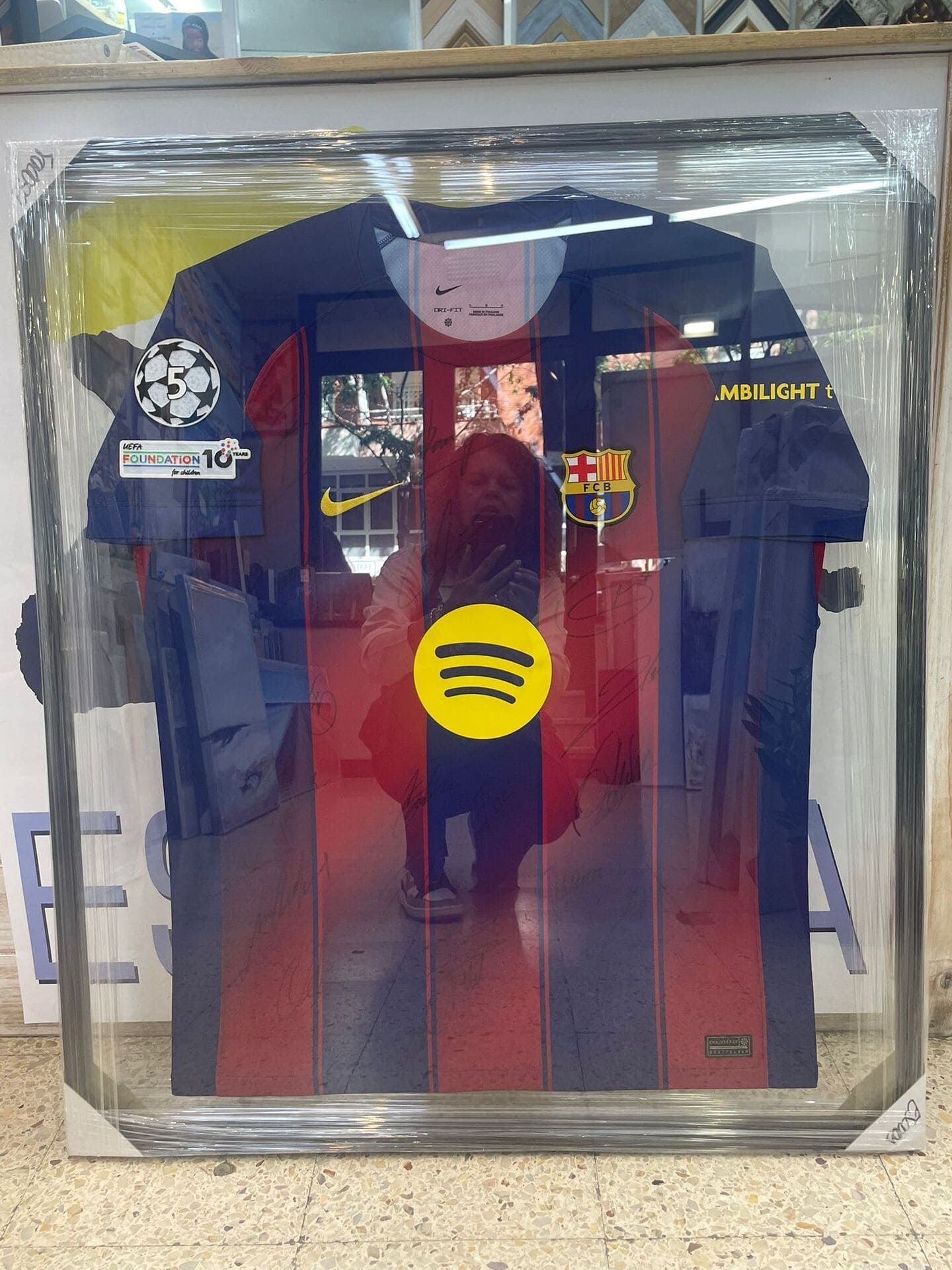 Camiseta de Spotify enmarcada en rojo oscuro y azul marino, envasada en plástico transparente.