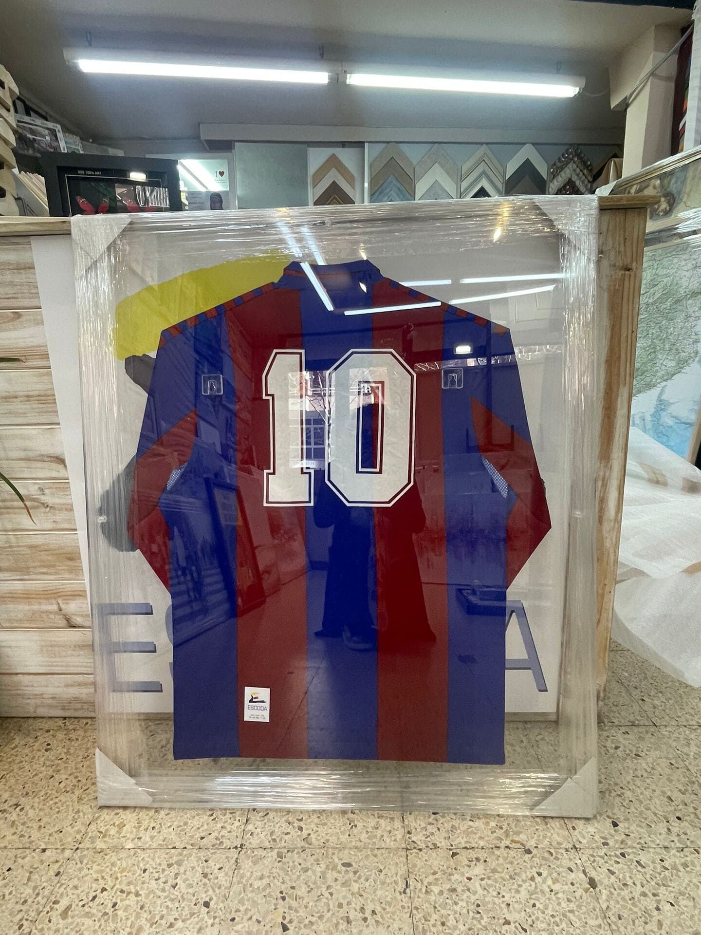 Camiseta enmarcada a rayas rojas y azules con el número 10, visible detrás de una envoltura de plástico transparente.