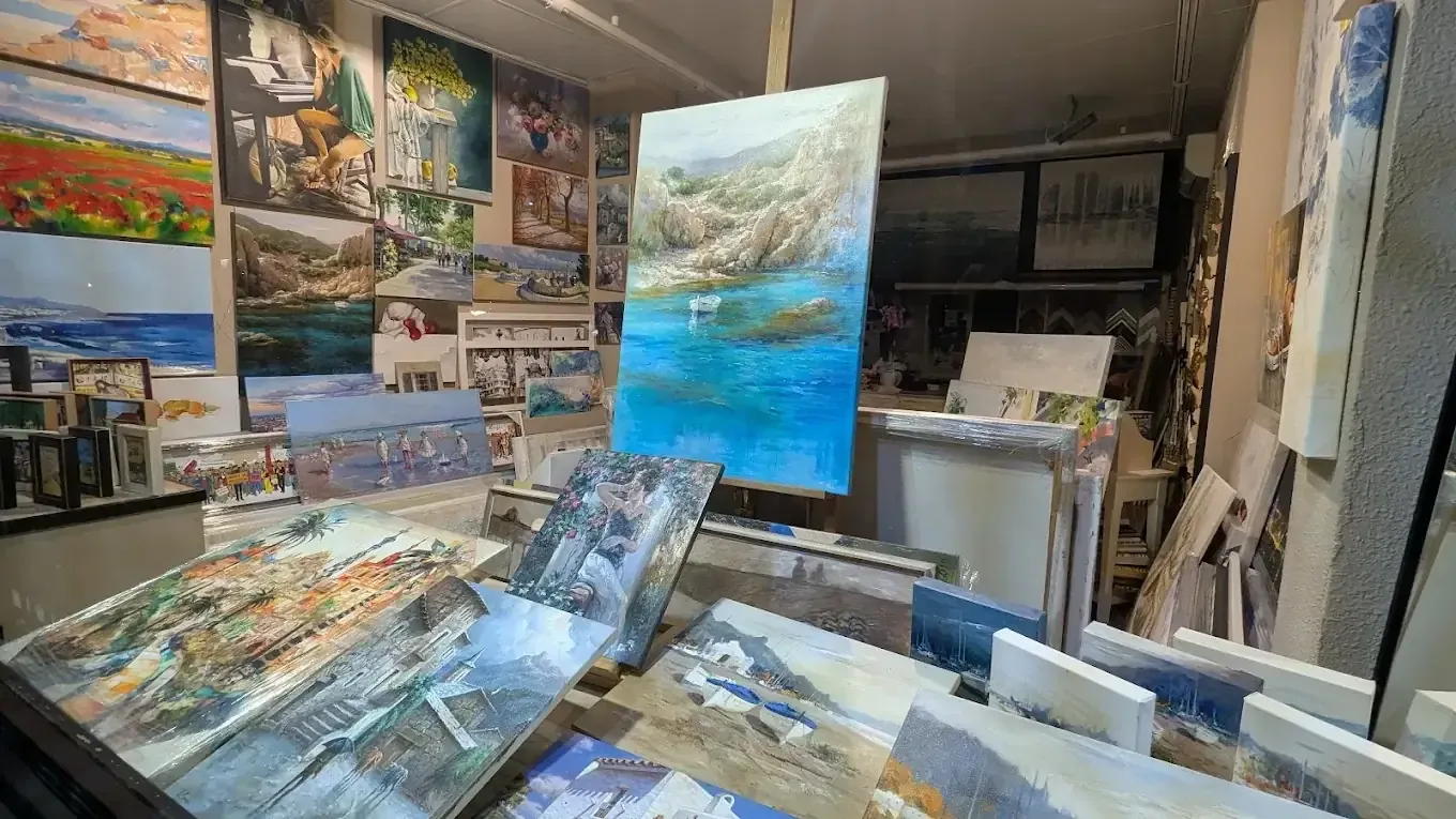 Un estudio de arte repleto de cuadros de paisajes con mares azules y escenas costeras en exposición.