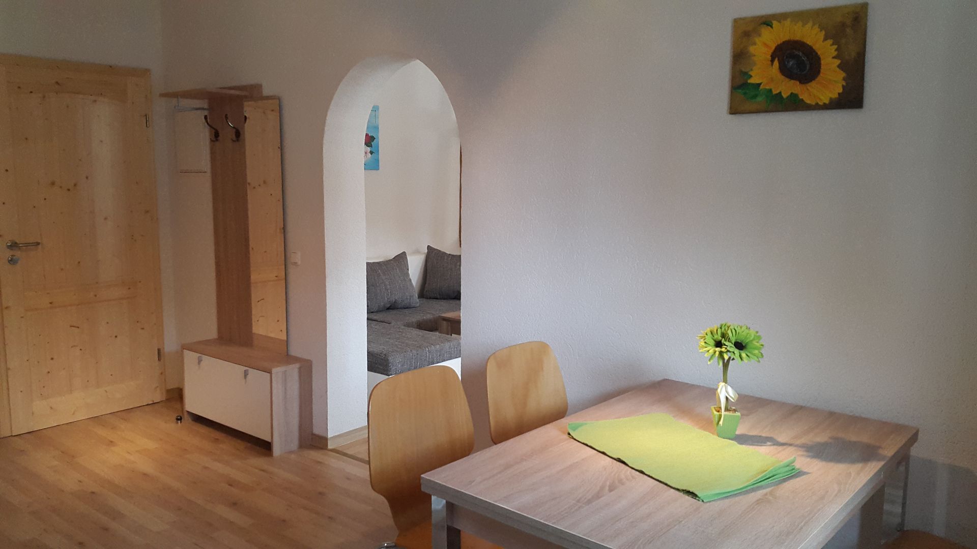 Essbereich mit Holztisch, grüner Deko und Torbogen zum ruhigen Wohnbereich.