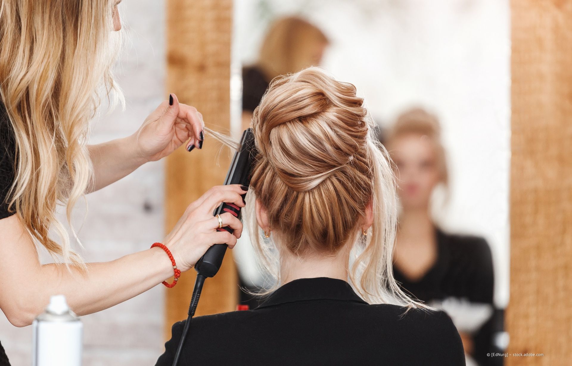 Frau lässt sich im Salon die Haare stylen; Stylistin benutzt ein Glätteisen für blondes Haar.