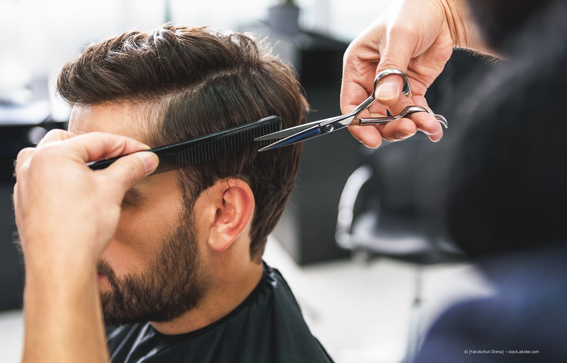 Friseur schneidet einem Mann in einem Salon mit Schere und Kamm die Haare.