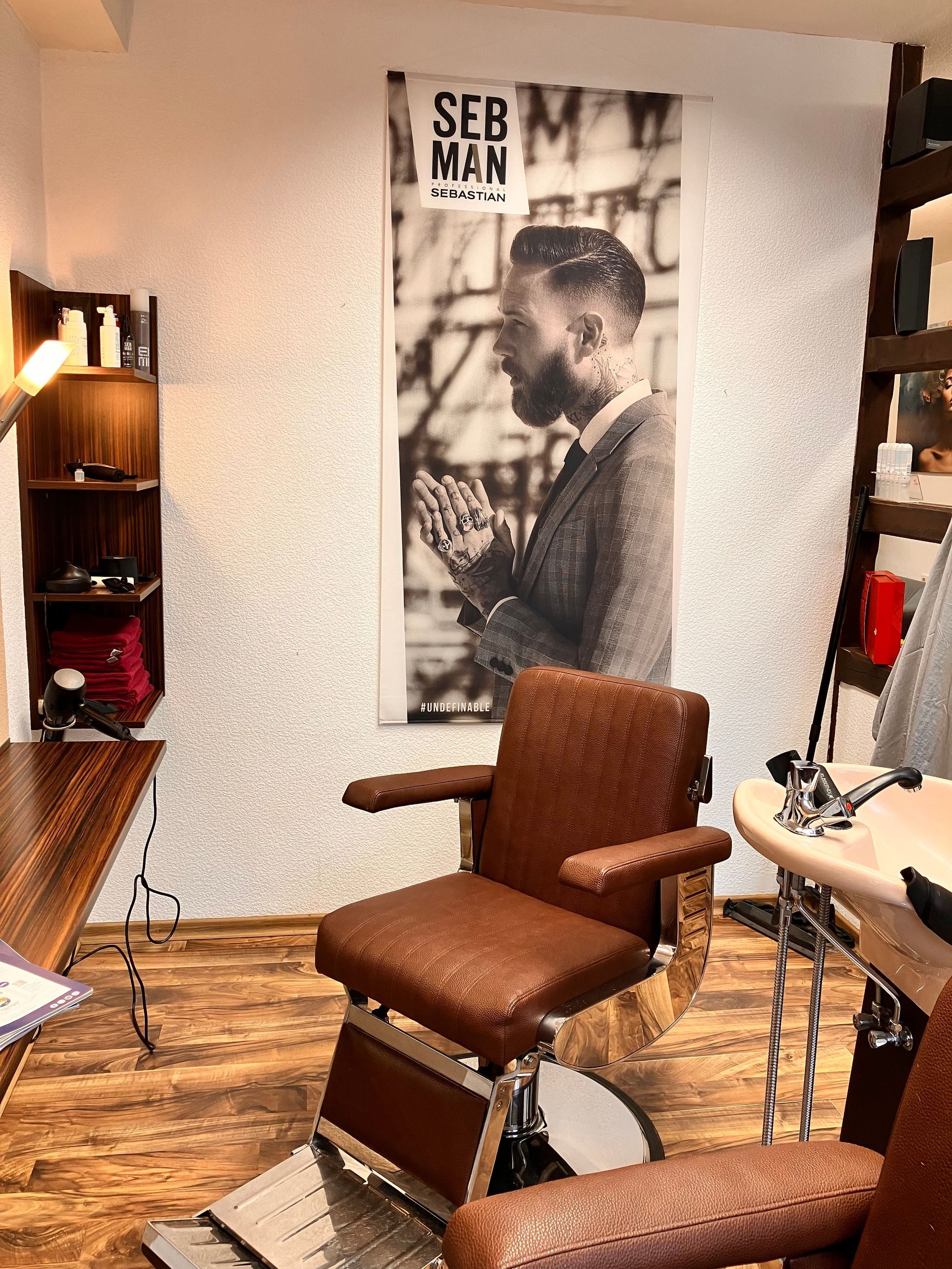 Inneneinrichtung eines Friseursalons mit braunem Friseurstuhl, Holzboden und Seb Man-Werbung.
