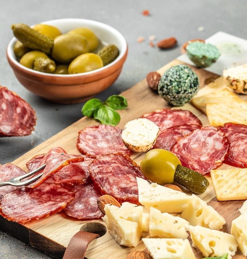 Una tabla de cortar de madera cubierta con carne, queso, encurtidos y nueces.