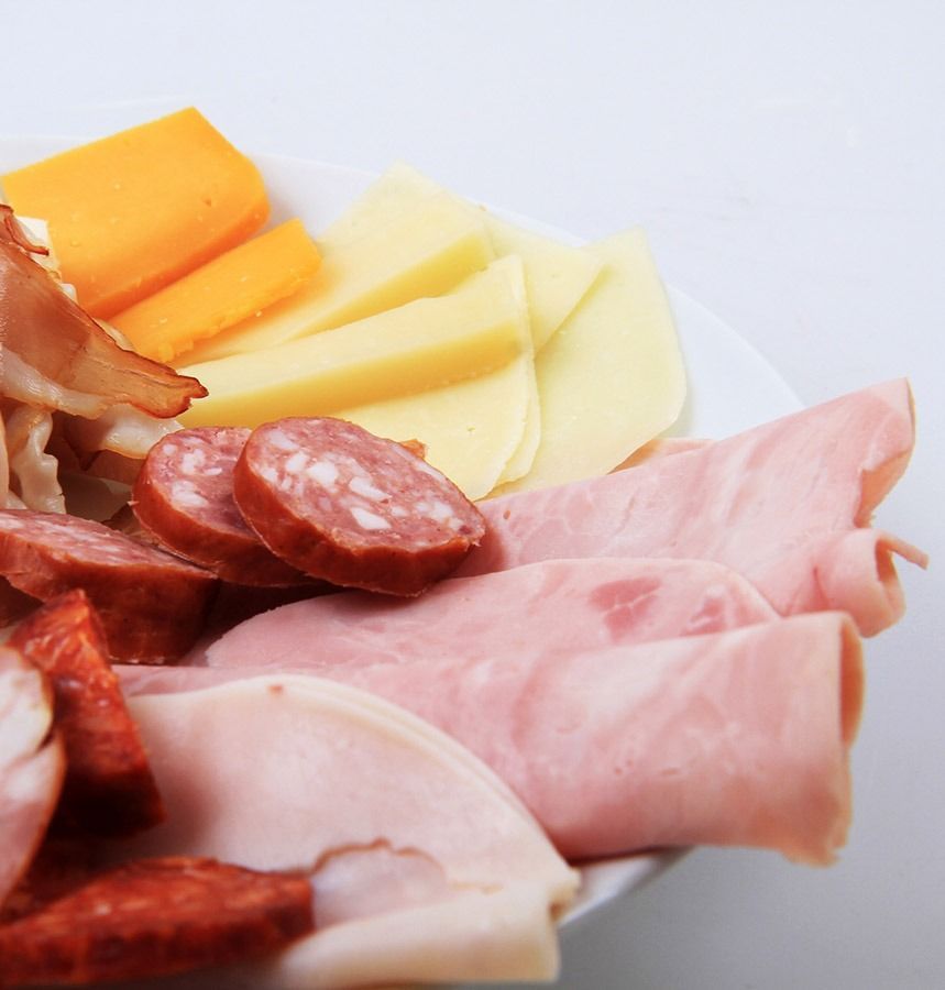 Un plato blanco cubierto con jamón, queso y salchicha.