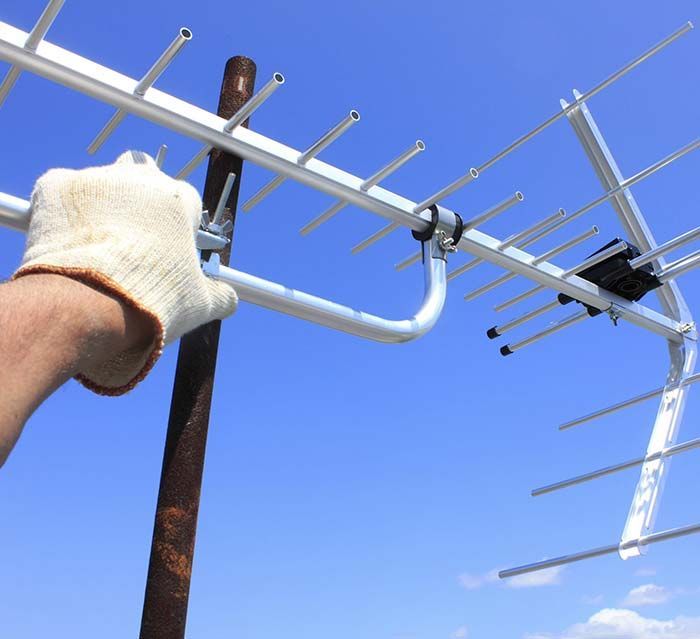 Una mano enguantada sostiene una antena de televisión contra un cielo azul.