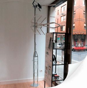 Alta antena metálica dentro de un edificio, cerca de una ventana con vistas a la calle.