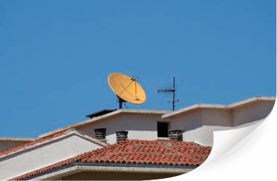 Antena parabólica amarilla y antena en un tejado con tejas rojas contra un cielo azul.