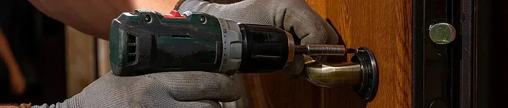 Una persona usa un taladro para instalar una cerradura. Lleva guantes de trabajo y el entorno es interior.