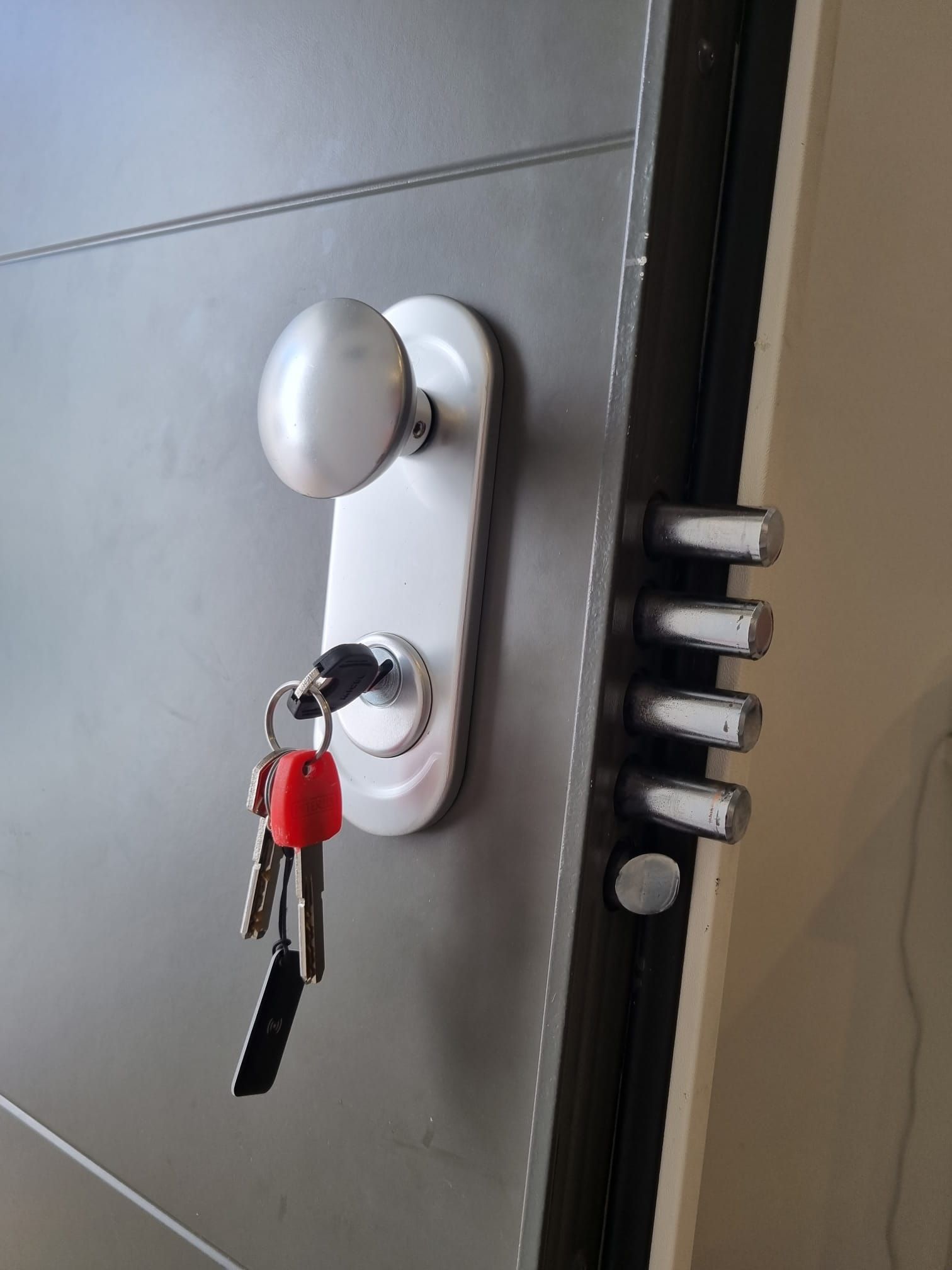 Puerta gris con manija plateada, llave insertada en la cerradura, llaves colgando debajo.