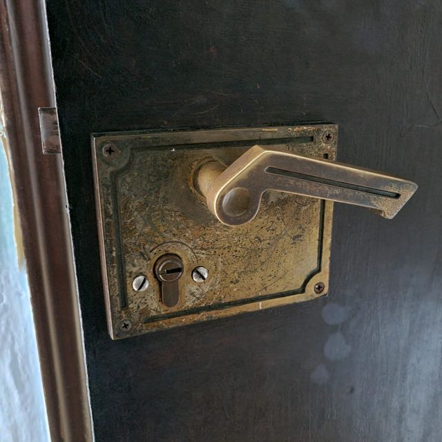 Manija de puerta de latón con ojo de cerradura y placa posterior cuadrada en una puerta oscura.