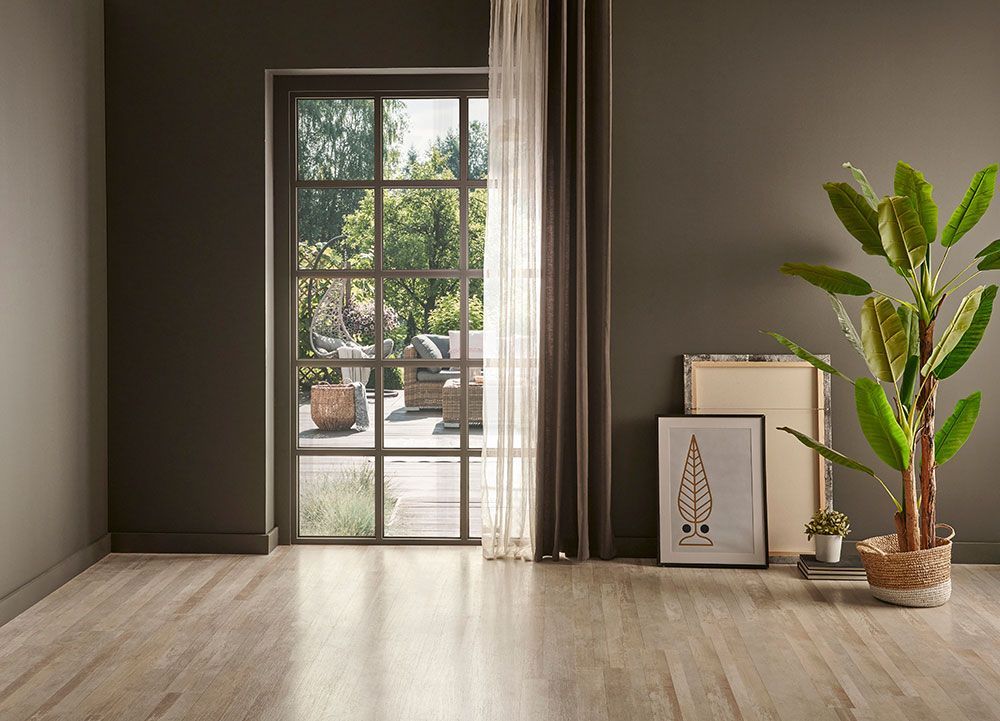 Leerer Raum mit dunkelgrauen Wänden, großem Fenster zum Garten, Holzboden, Pflanze und gerahmter Kunst.