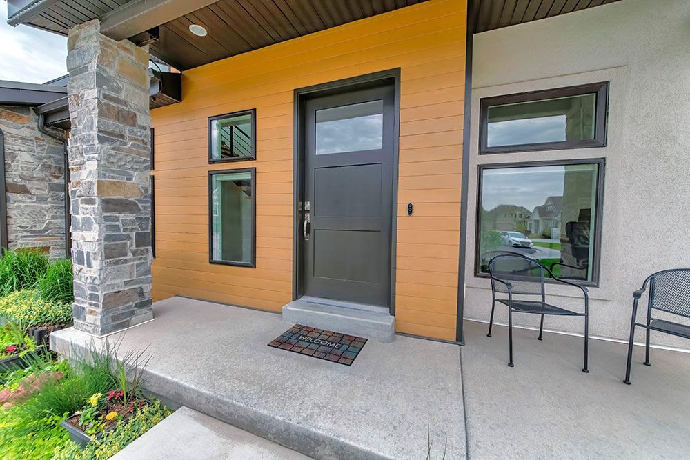 Moderner Hauseingang mit dunkler Tür, Fenstern und Steinsäulen.