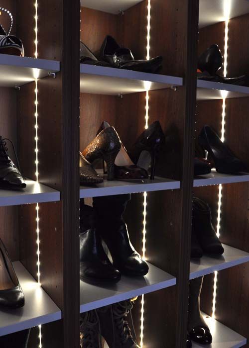 Schuhregale mit verschiedenen Schuhen, beleuchtet durch vertikale Lichterketten in einem Holzschrank.