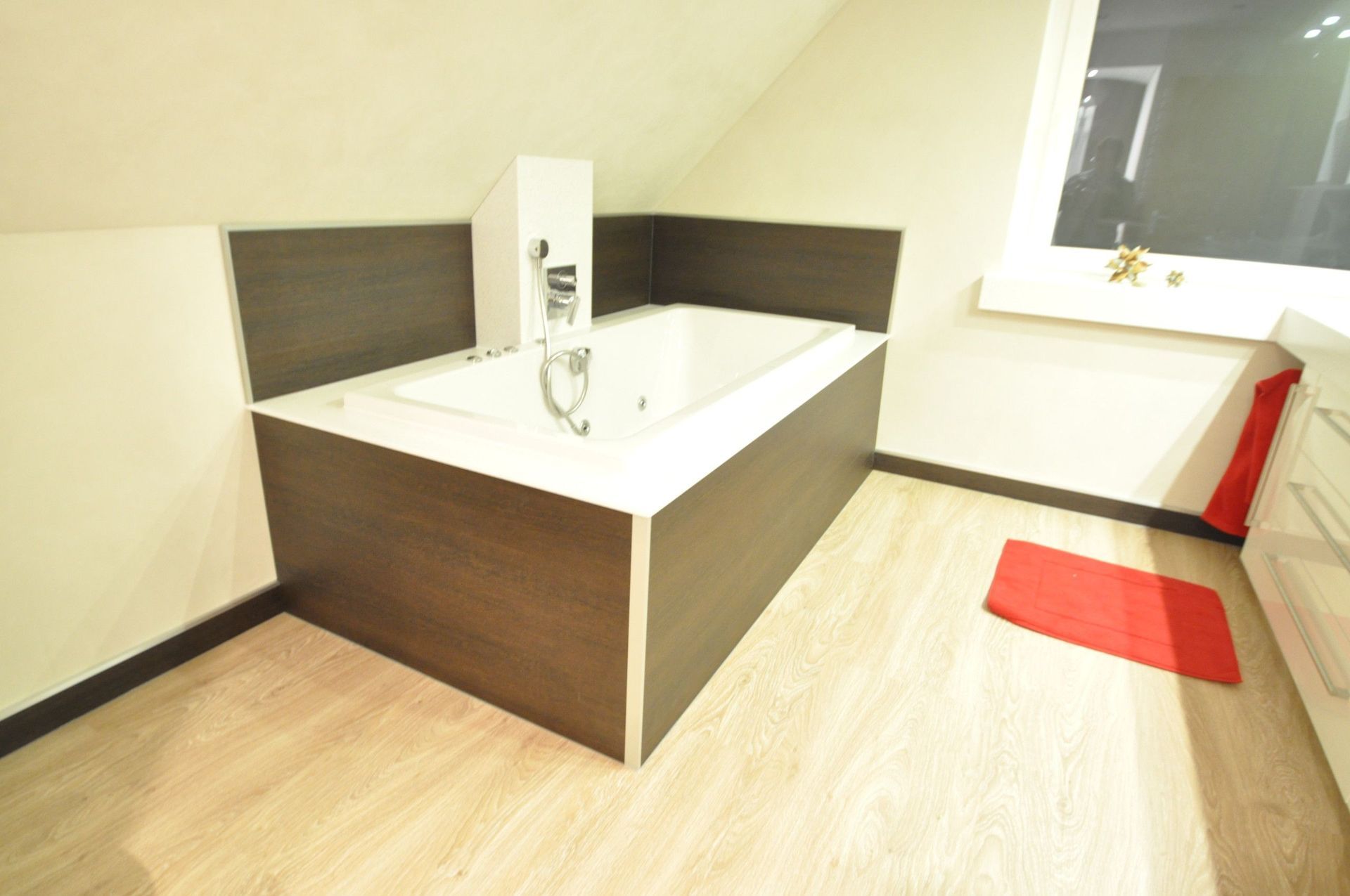 Badezimmer mit eingebauter Badewanne und Fenster. Farbschema in Braun und Weiß mit roter Badematte.