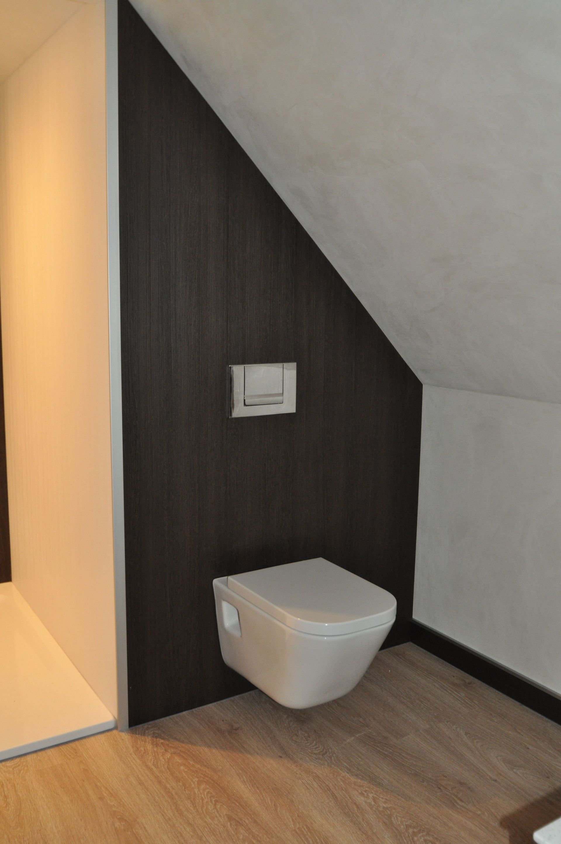 Weißes Wand-WC in einem kleinen Badezimmer mit dunkler Holzakzentwand unter einer schrägen Decke.