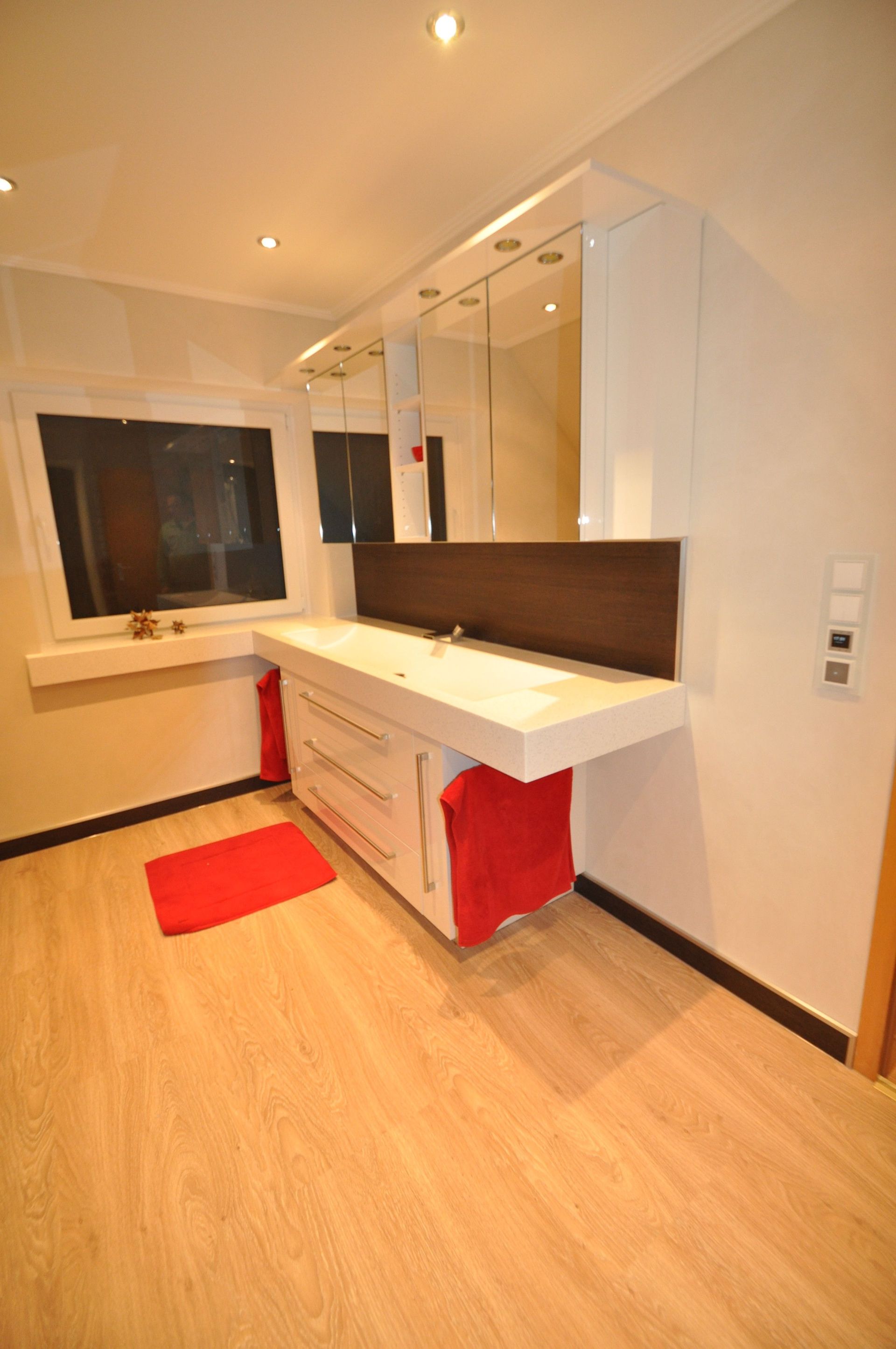 Weißer Waschtisch mit Schubladen, Spiegel, roten Handtüchern in einem Badezimmer mit Holzboden.
