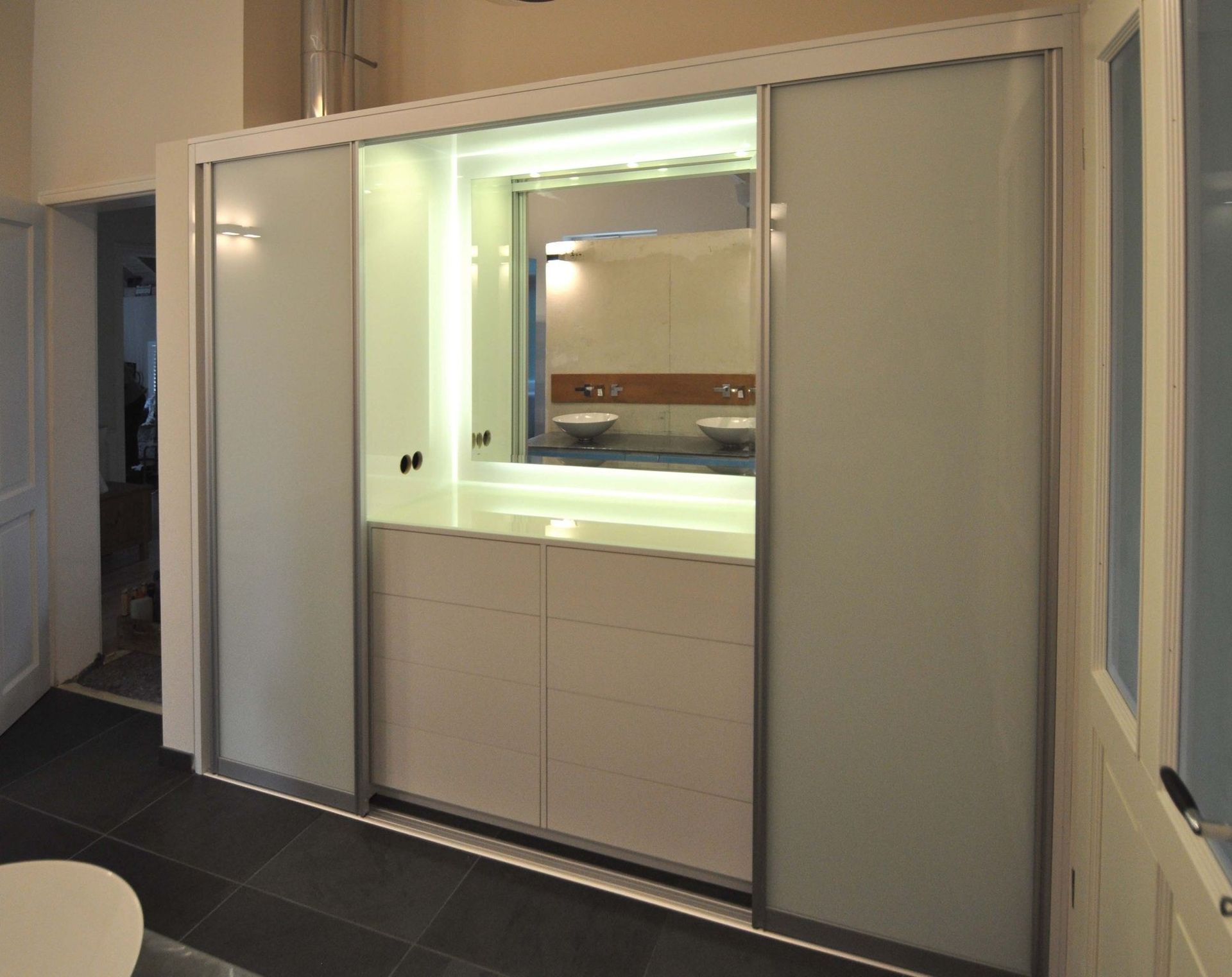 Weißer Badezimmerwaschtisch mit mattierten Schiebetüren, einem Spiegel und Schubladen.