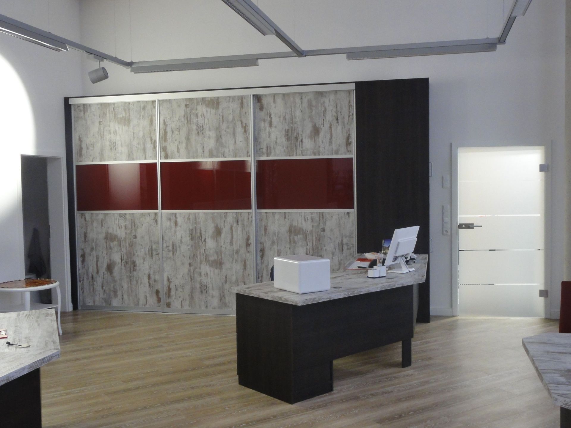 Innenraum eines Ausstellungsraums mit einem modernen Schreibtisch, einem großen Schrank mit roten Paneelen.