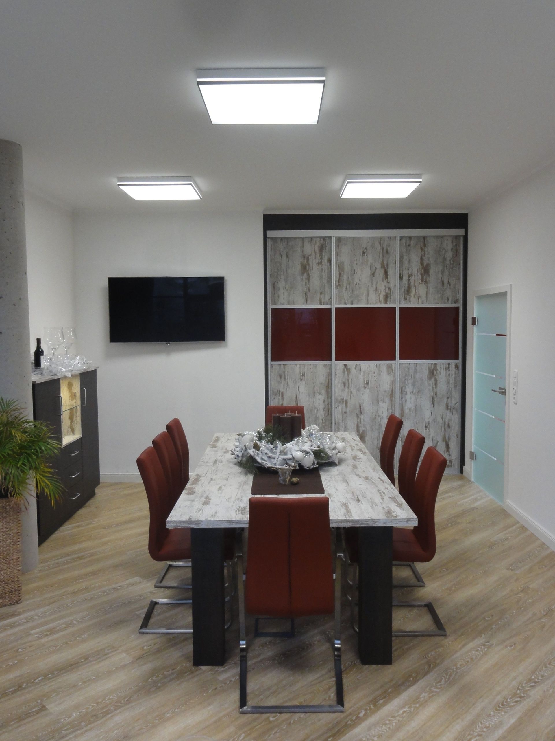 Esszimmer mit langem Tisch, roten Stühlen und einem großen Kleiderschrank. Heller Holzboden.