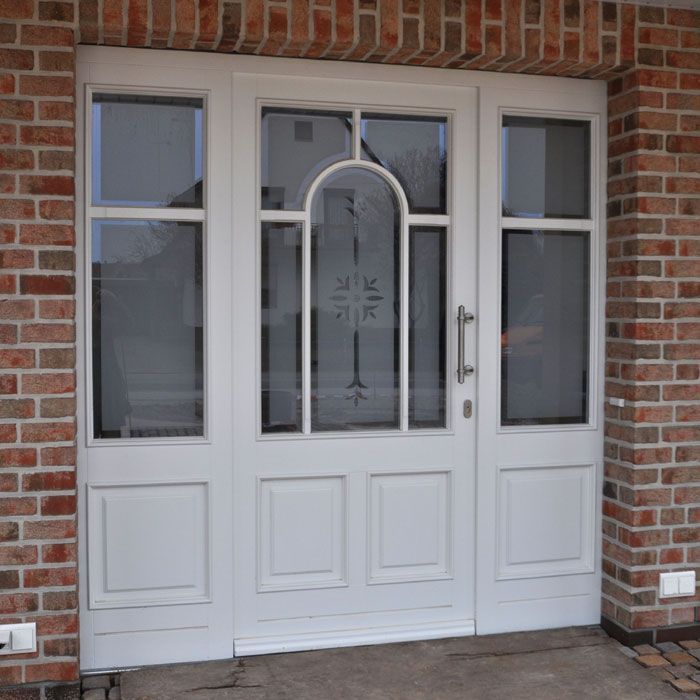 Weiße Tür mit Glaseinsätzen, eingelassen in eine rote Backsteinmauer.