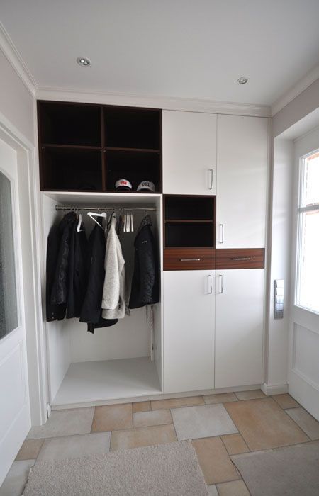 Einbauschrank mit Garderobe, Regalen und Schränken in einem Flur. Weiß und Braun mit hängenden Mänteln.
