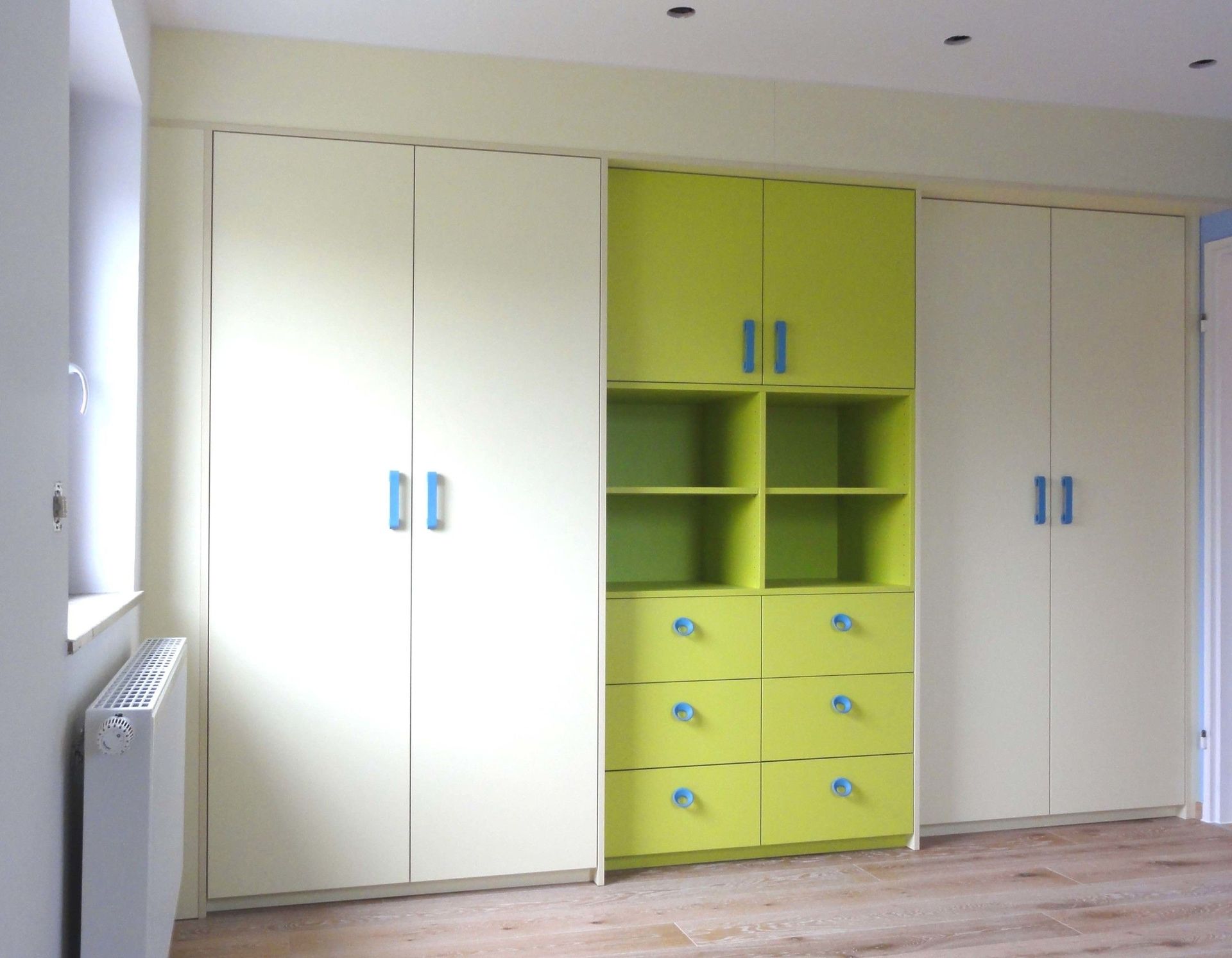 Eine Reihe Einbauschränke mit weißen und limettengrünen Schränken und blauen Griffen.
