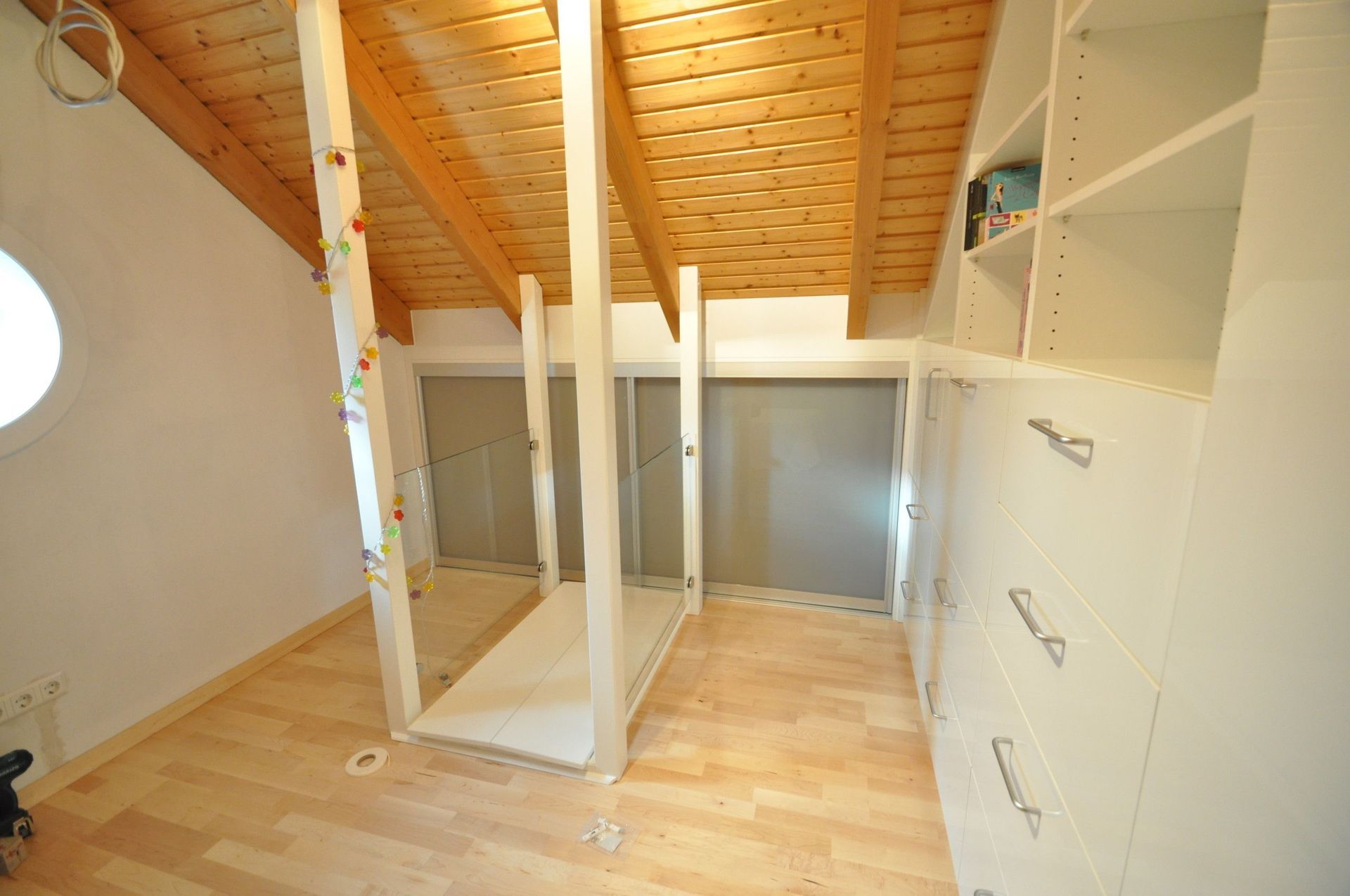 Schlafzimmer mit Dachschräge, Holzbalken, eingebauten weißen Regalen und einem Bettgestell in der Mitte.