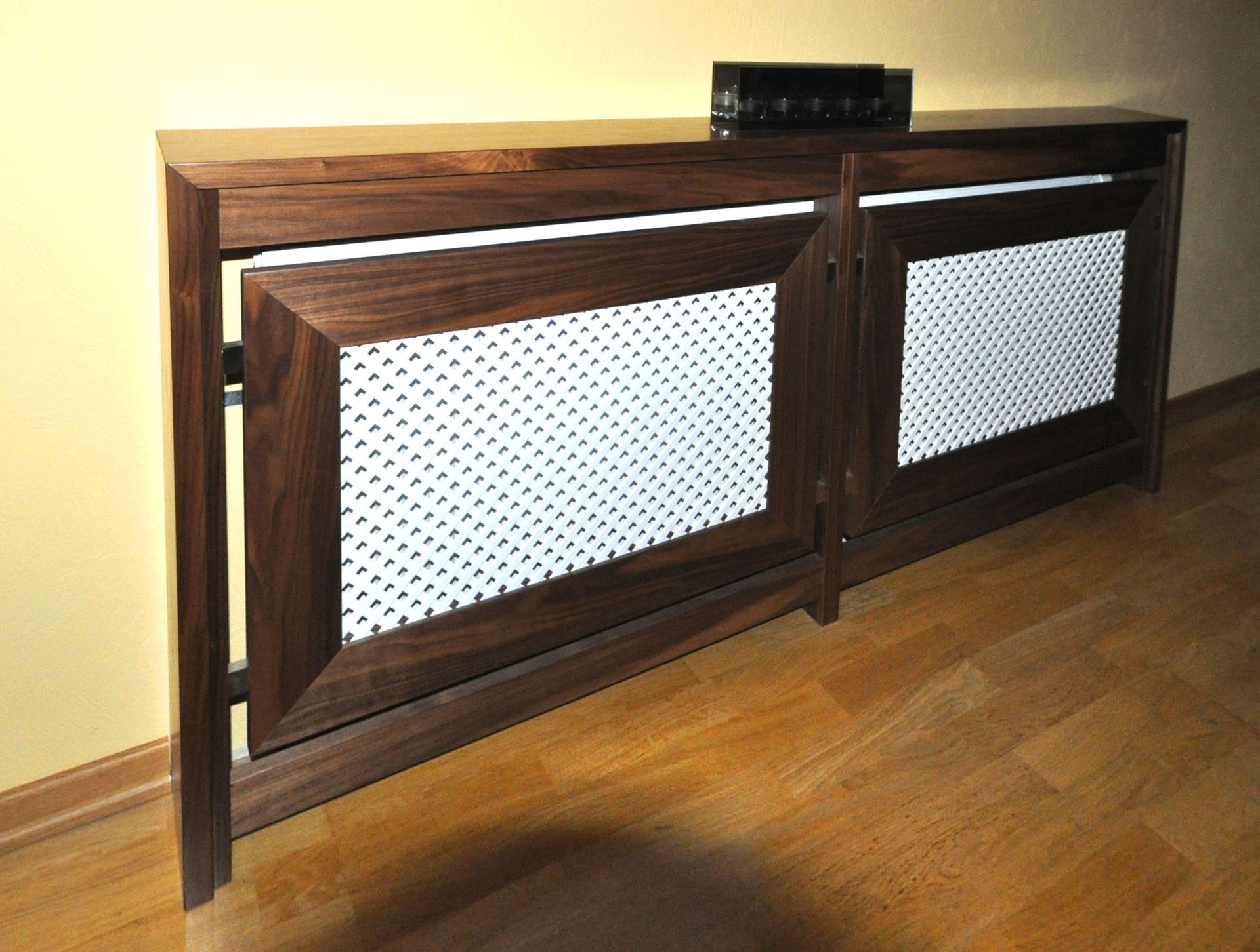 Dunkles Holzgehäuse mit weißen Lochplatten. Oben befindet sich ein kleines elektronisches Gerät.