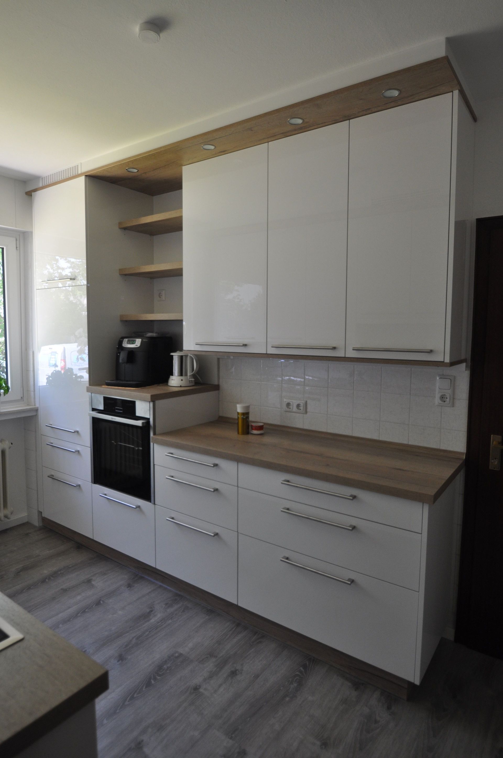 Weiße, moderne Küche mit Arbeitsplatten und Schränken aus Holz, eingebautem Ofen und offenen Regalen.