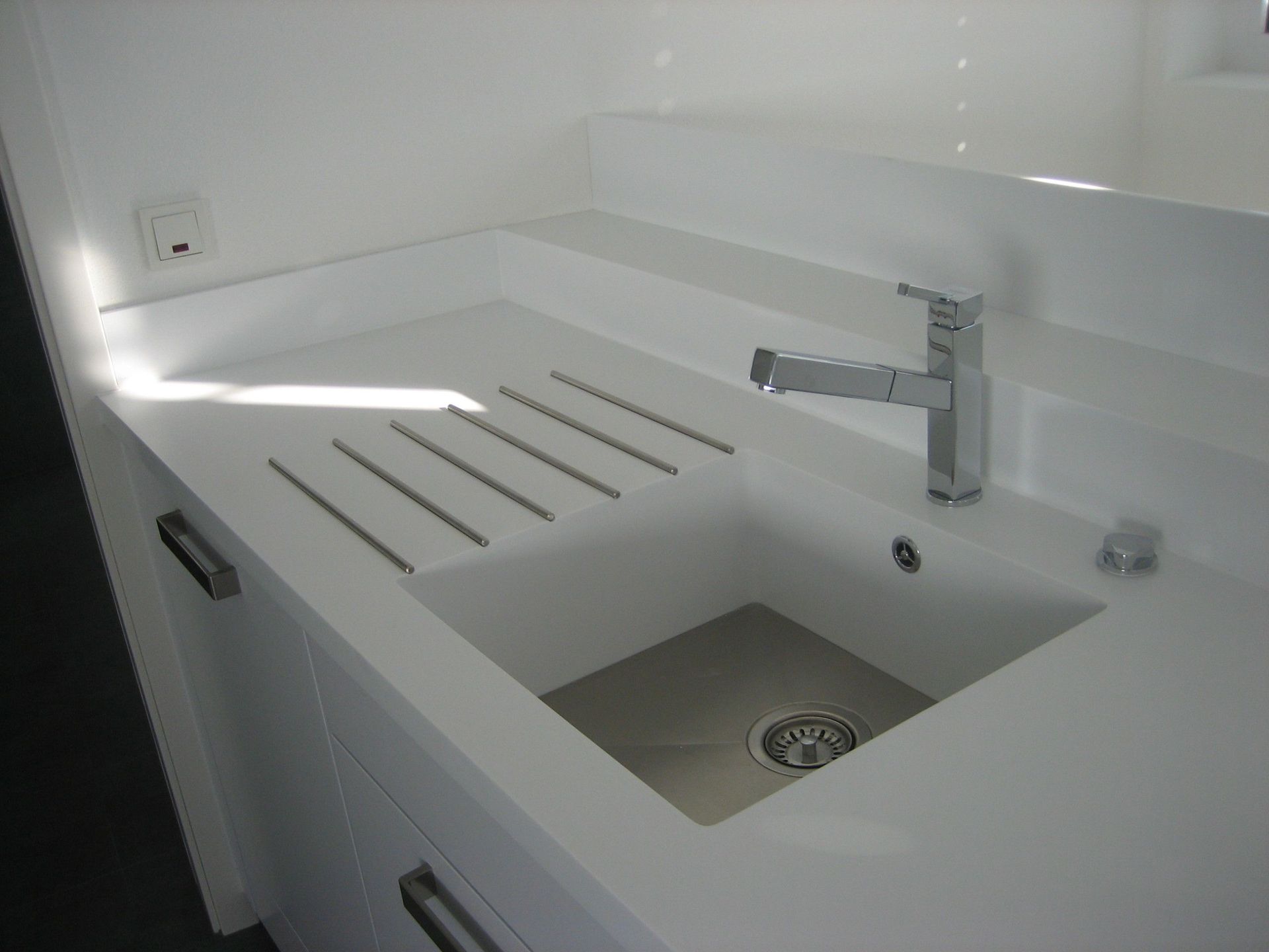 Weißes Spülbecken mit Edelstahlhahn und Abtropffläche, in die weiße Arbeitsplatte integriert.