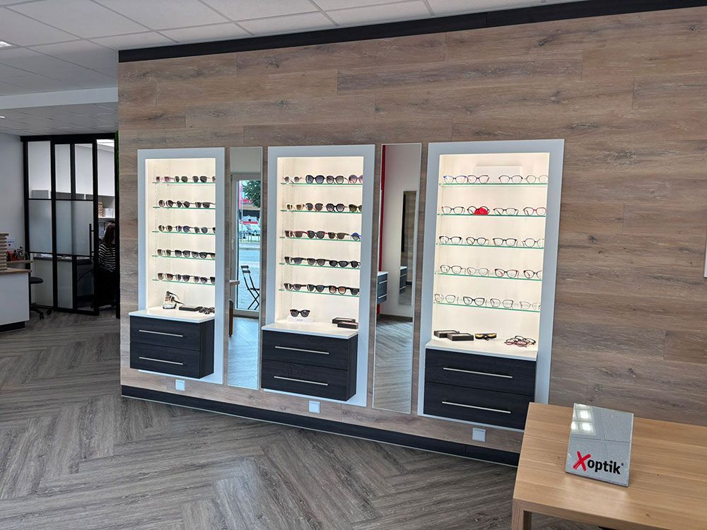 Brillenvitrinen in einer Optikerpraxis, Holzvertäfelung, mit ausgestellten Brillen und einem Holztisch.