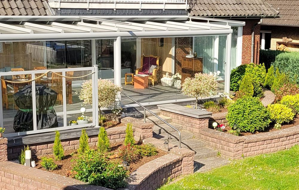 Wintergarten mit Glaswänden, an ein Backsteinhaus angebaut, mit Blick auf einen angelegten Garten.
