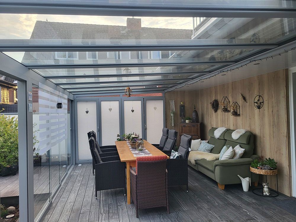 Überdachter Essbereich im Freien mit Glasdach, Holzboden und Sitzgelegenheiten für eine Gruppe.