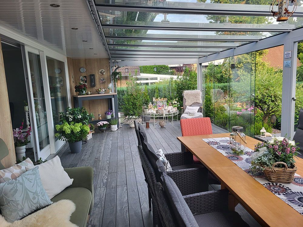 Überdachte Außenterrasse mit Glasdach, Esstisch, Sitzgelegenheiten und Blick auf den Garten.
