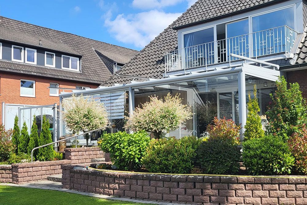 Ein Haus mit gemauerter Terrasse, Garten und Metallbalkon unter einem strahlend blauen Himmel.