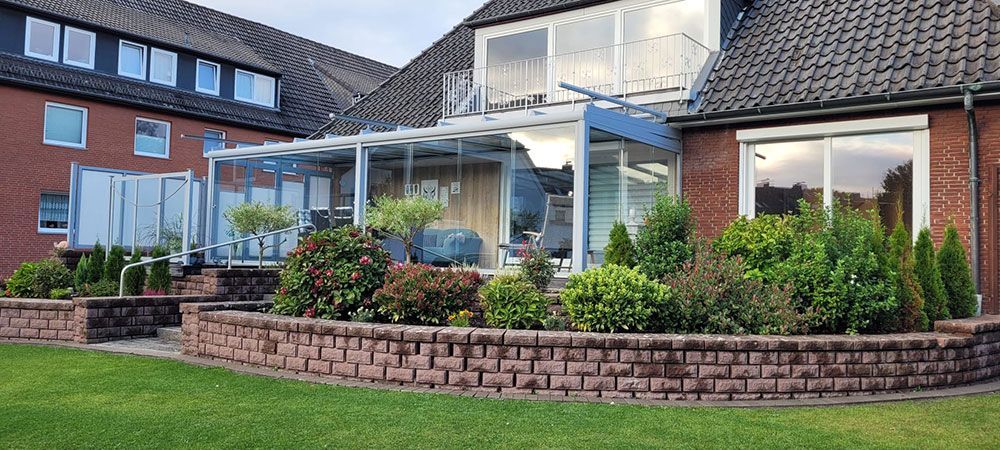 Backsteinhaus mit Wintergarten aus Glas, gemauertem Gartenbeet und grünem Rasen.