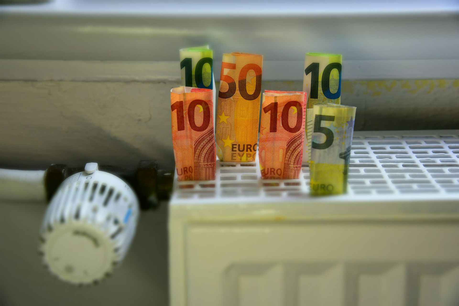 An einem Heizkörper befestigte Euro-Banknoten, im Vordergrund ein Thermostatknopf.