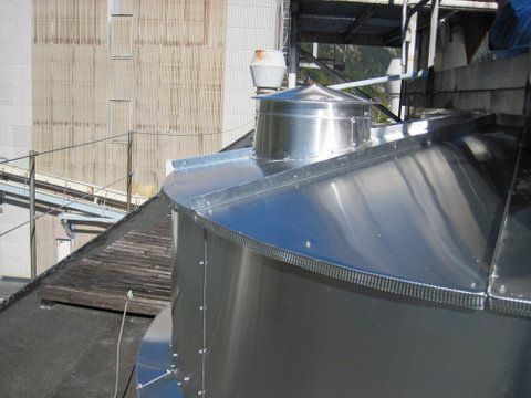 Industrietank aus Edelstahl mit belüftetem Deckel auf einem Dach neben einem Gehweg und einer Gebäudewand.