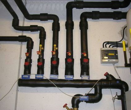 Schwarze, an der Wand montierte Rohre und Ventile mit einem kleinen elektrischen Schaltkasten in einem Hauswirtschaftsraum.