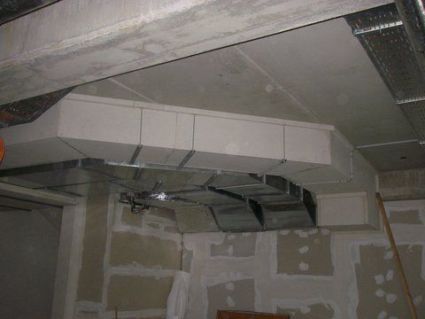 Beschädigte Decke mit freiliegenden Lüftungskanälen und herabhängenden Metallplatten in einem unfertigen Raum